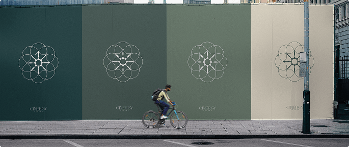 Street view of a cyclist passing by a long wall with Cinergy Spaces logos on green and beige panels.